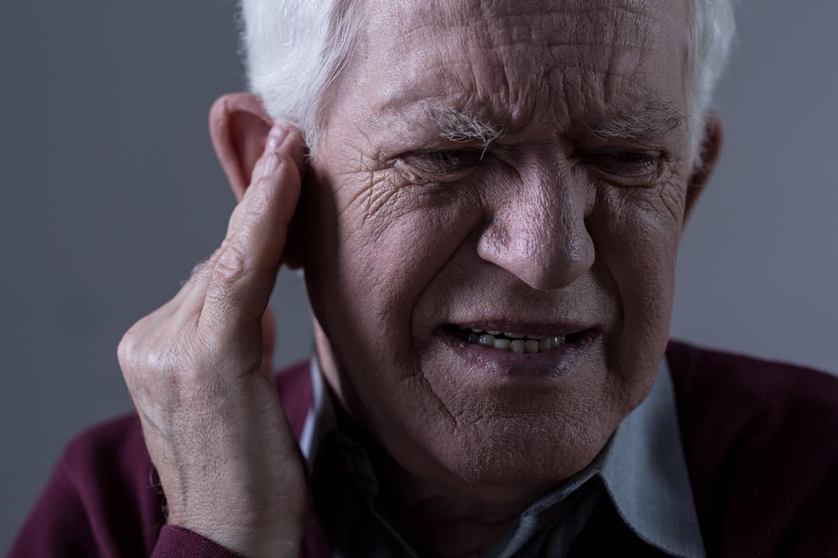 senior man in pain holding ear from tinnitus